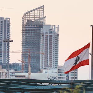 Urban skyline of Beirut with a prominent Lebanese flag gently waving at sunset.
