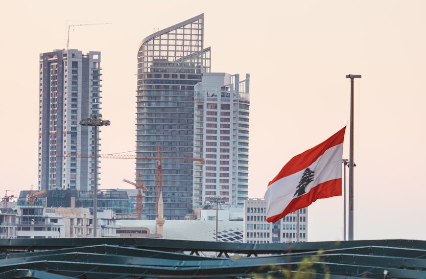 Urban skyline of Beirut with a prominent Lebanese flag gently waving at sunset.
