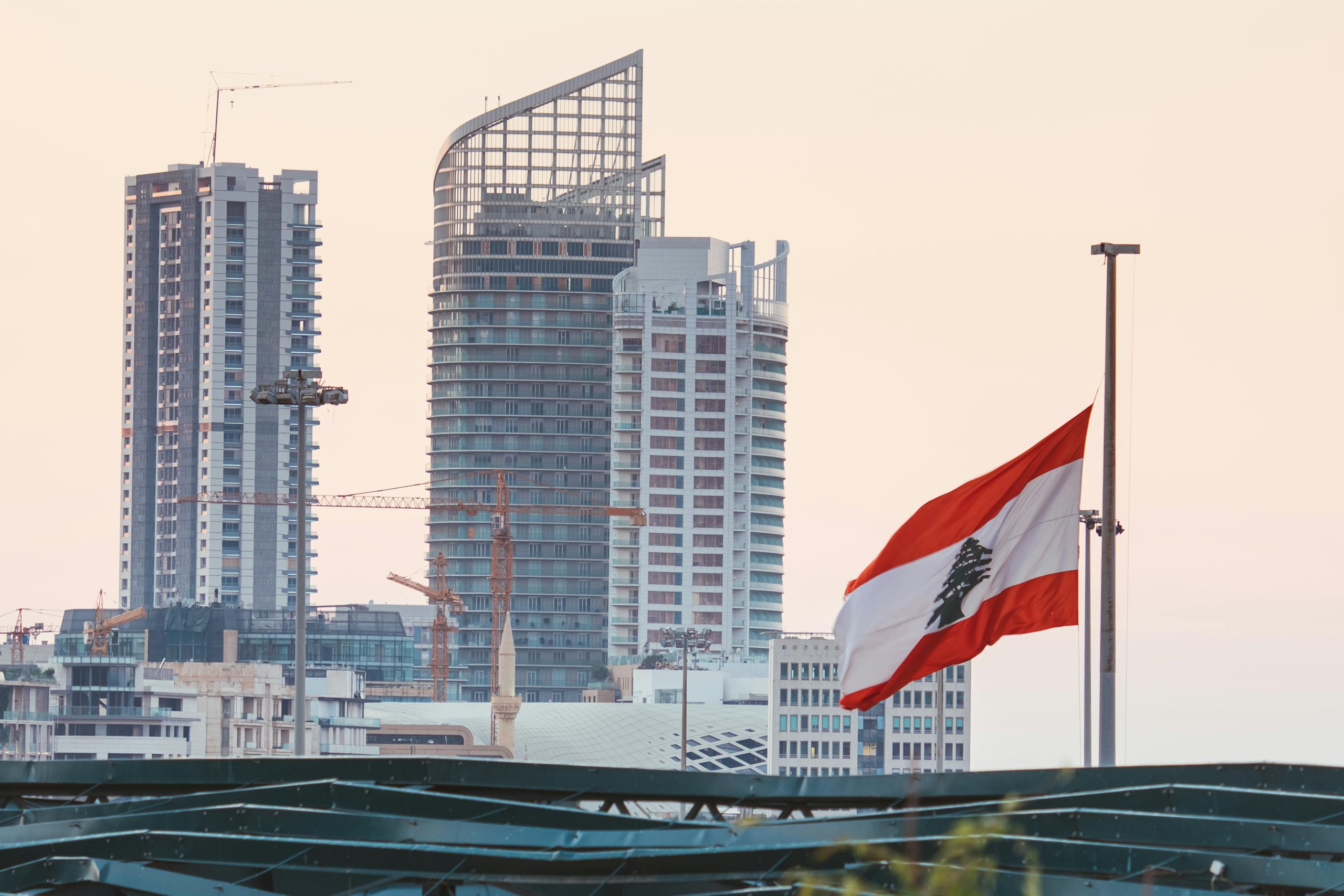 Urban skyline of Beirut with a prominent Lebanese flag gently waving at sunset.